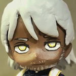 Image of a custom nendoroid chibi doll of Eilhart. He is depicted as a dark skinned man with yellow-gold eyes with white pupils, grey-ish white shoulder-length hair tied back in a half-ponytail. He is wearing the nendoroid doll priest outfit set, which consists of a black cassock, pants, and black loafers, alongside a white and gold stole with a cross motif. the doll is posed with its hand stretched out to the viewer. 